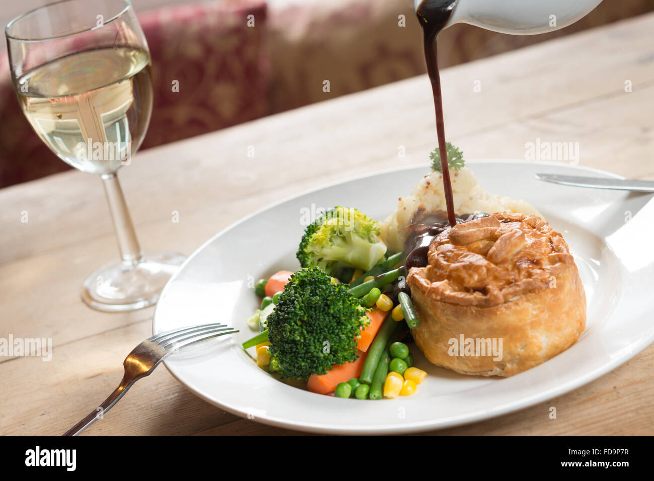 Pie und Kartoffelpüree und Gemüse auf einem Teller mit Soße gegossen und mit einem Glas Wein. Ein Pub-Essen. Stockfoto