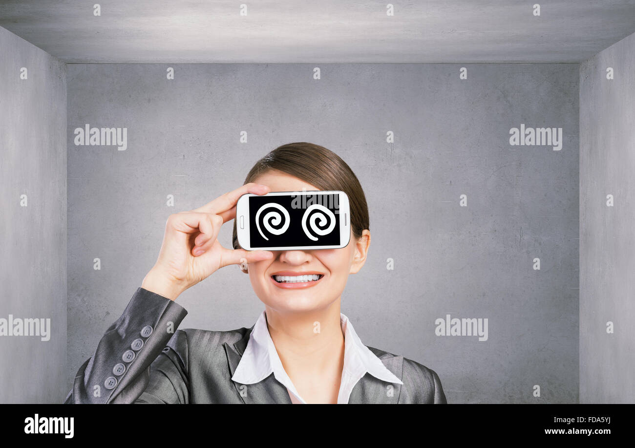 Schöne junge Frau mit Handy gegen ihre Augen Stockfoto