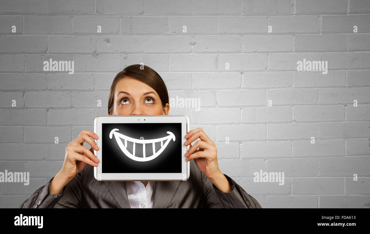 Schöne junge Frau Holding Tablet mit Lächeln gegen ihren Mund Stockfoto