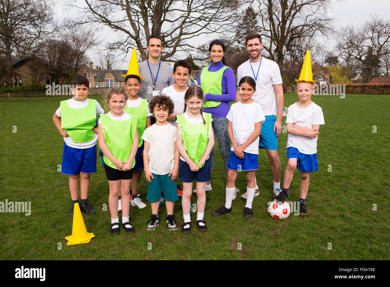 Ein Gruppenporträt einer Fußballmannschaft Kinder hinter ihnen sind ihre Trainer. Sie Lächeln und zwei der jungen kann man halten Stockfoto