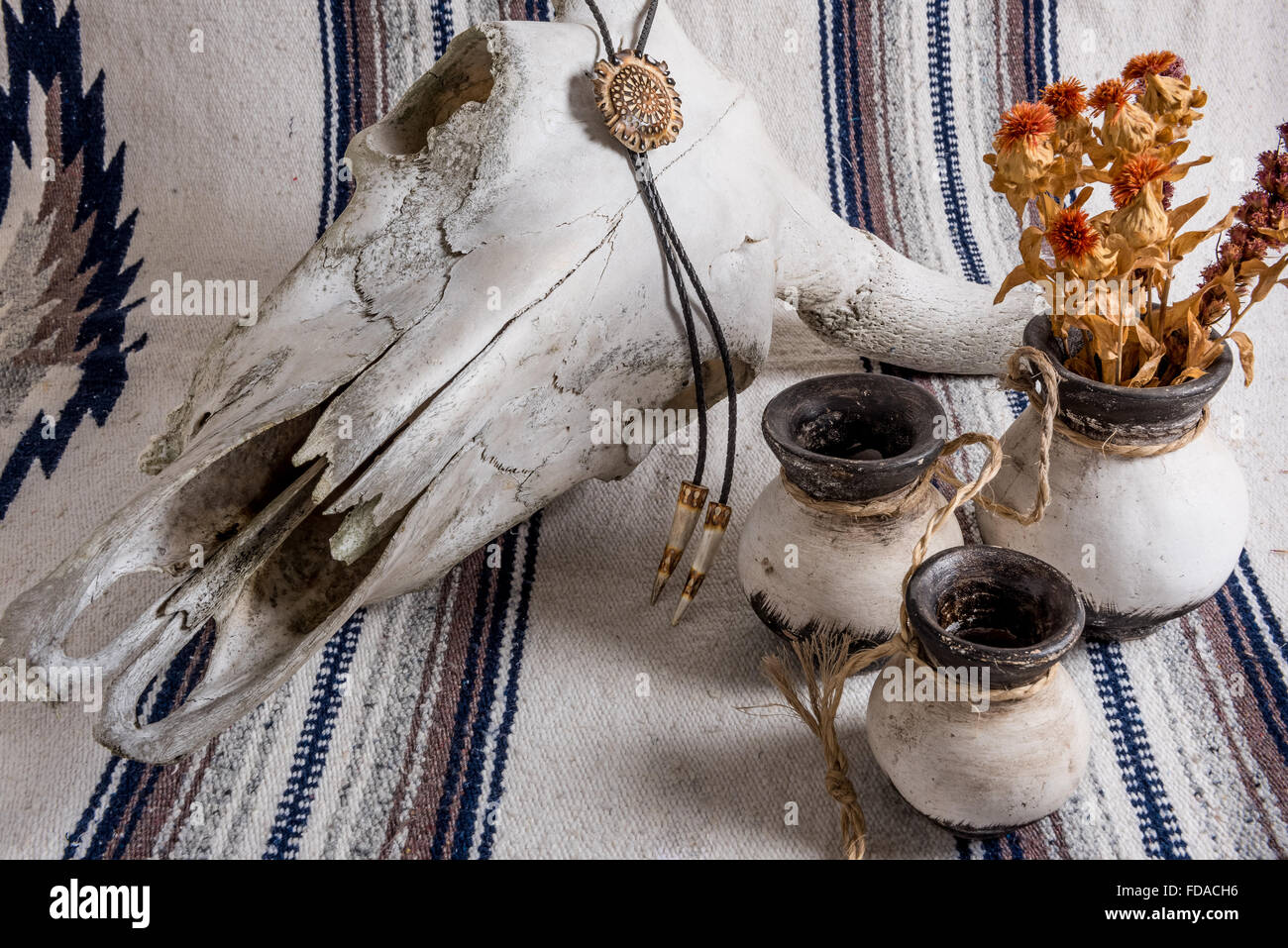 Verwitterter Kuhschädel drapiert mit einem geschnitzten Hirschgeweih bolo Krawatte, schwarz und weiß bemalte mexikanische Keramik mit getrockneten Blumen mexikanischen gestreiften Decke. Stockfoto