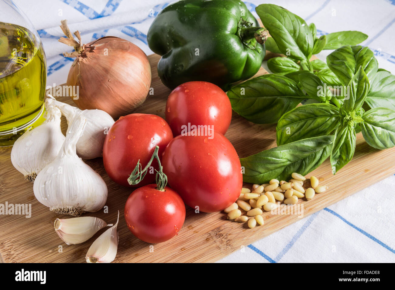 Frische italienische Zutaten, Knoblauch, Paprika, Tomaten, Zwiebel Basilikum und Pinienkerne auf einem Schneidebrett mit Olivenöl angeordnet. Stockfoto