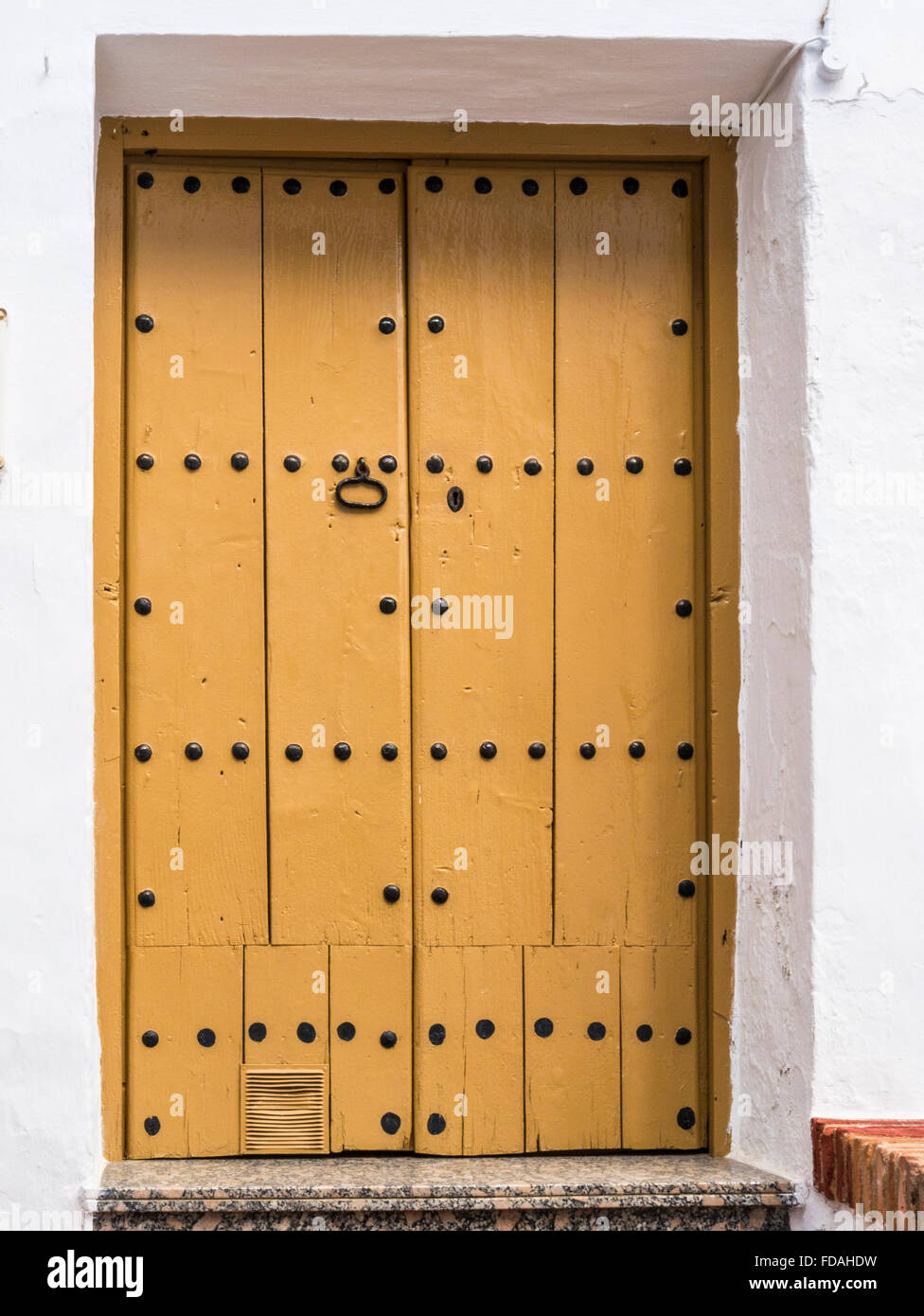 Gelbe Tür mit vertikaler Paneelverkleidung und Nieten und einem schmiedeeisernen Knopf/Griff, Frigiliana, Malaga, Andalusien, Spanien. Stockfoto