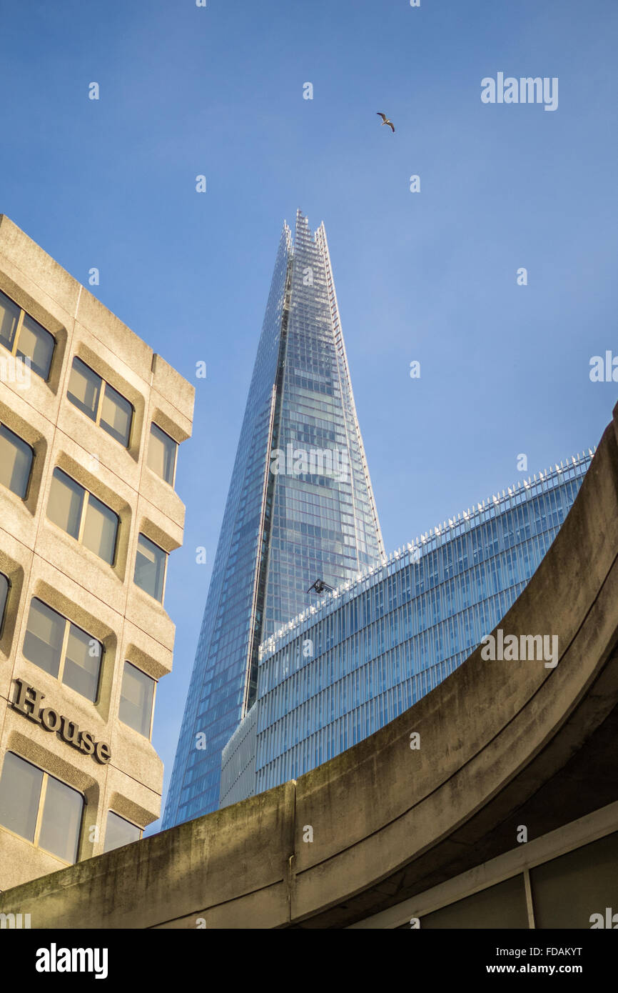 Der London-Shard flankiert von Betonbau Strukturen im Vordergrund mit ein Vogel fliegt durch einen klaren, blauen Himmel, Southwark London UK Stockfoto