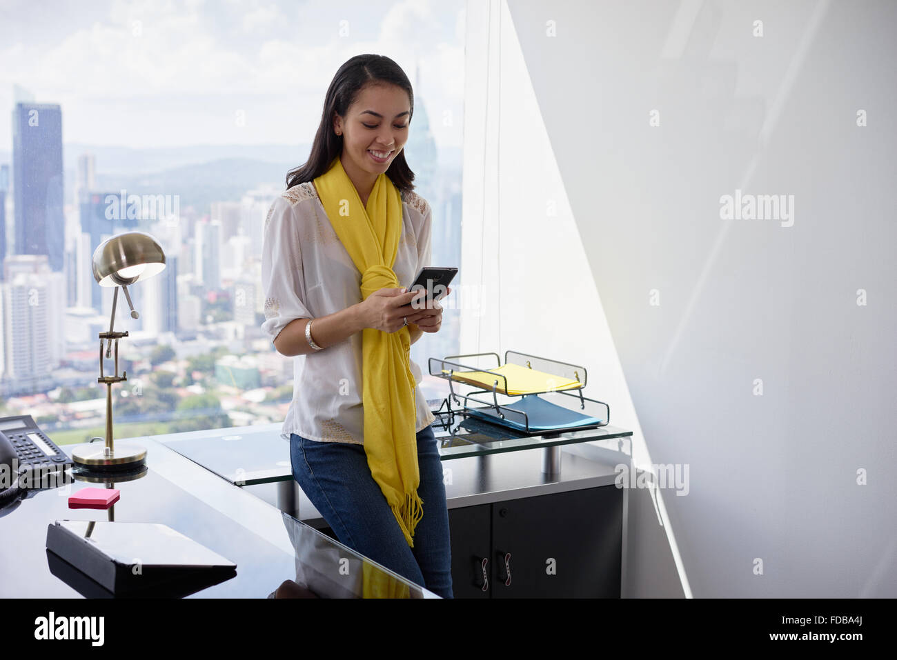 Multiethnische chinesische hispanischen Mädchen stützte sich auf Tabelle in ein modernes Bürogebäude mit Blick auf die Stadt im Hintergrund. Sie Stockfoto
