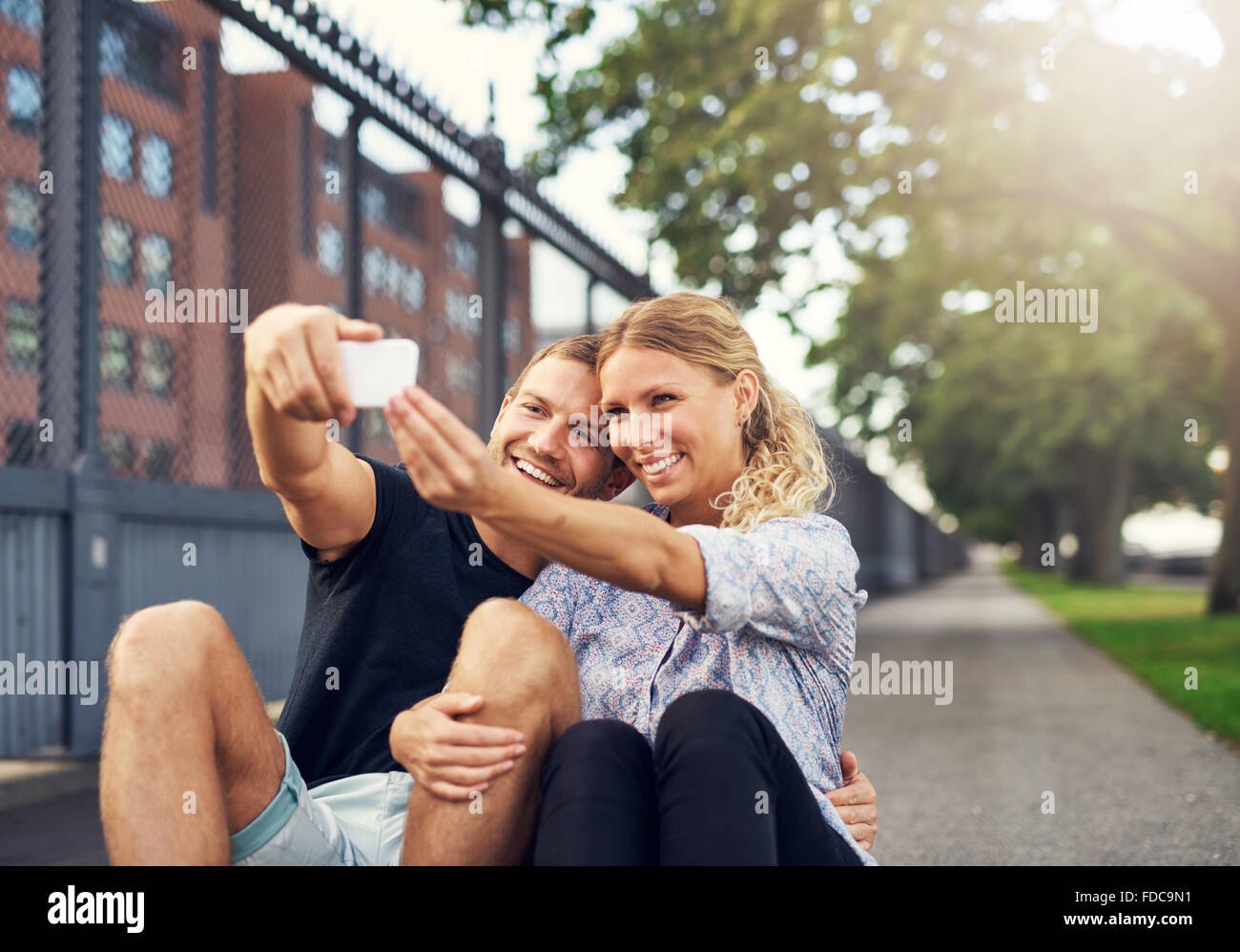 Glückliches Paar unter einem Selfie sitzt in einem Park in der Stadt Stockfoto