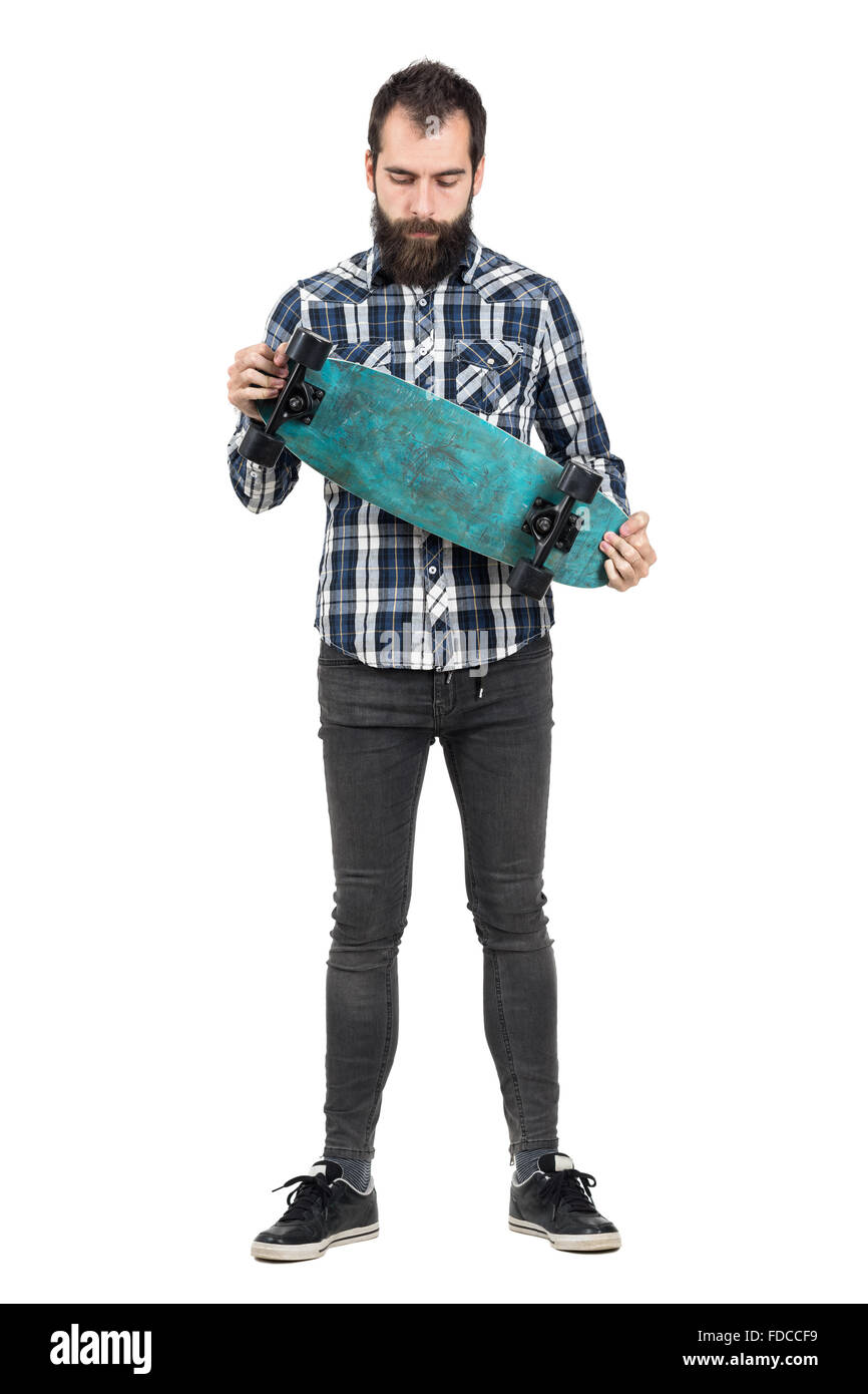 Junge Hipster in Tartan Shirt Skateboard auf der Suche nach unten halten. Ganzkörper-Länge-Porträt über weiße Studio-Hintergrund isoliert Stockfoto