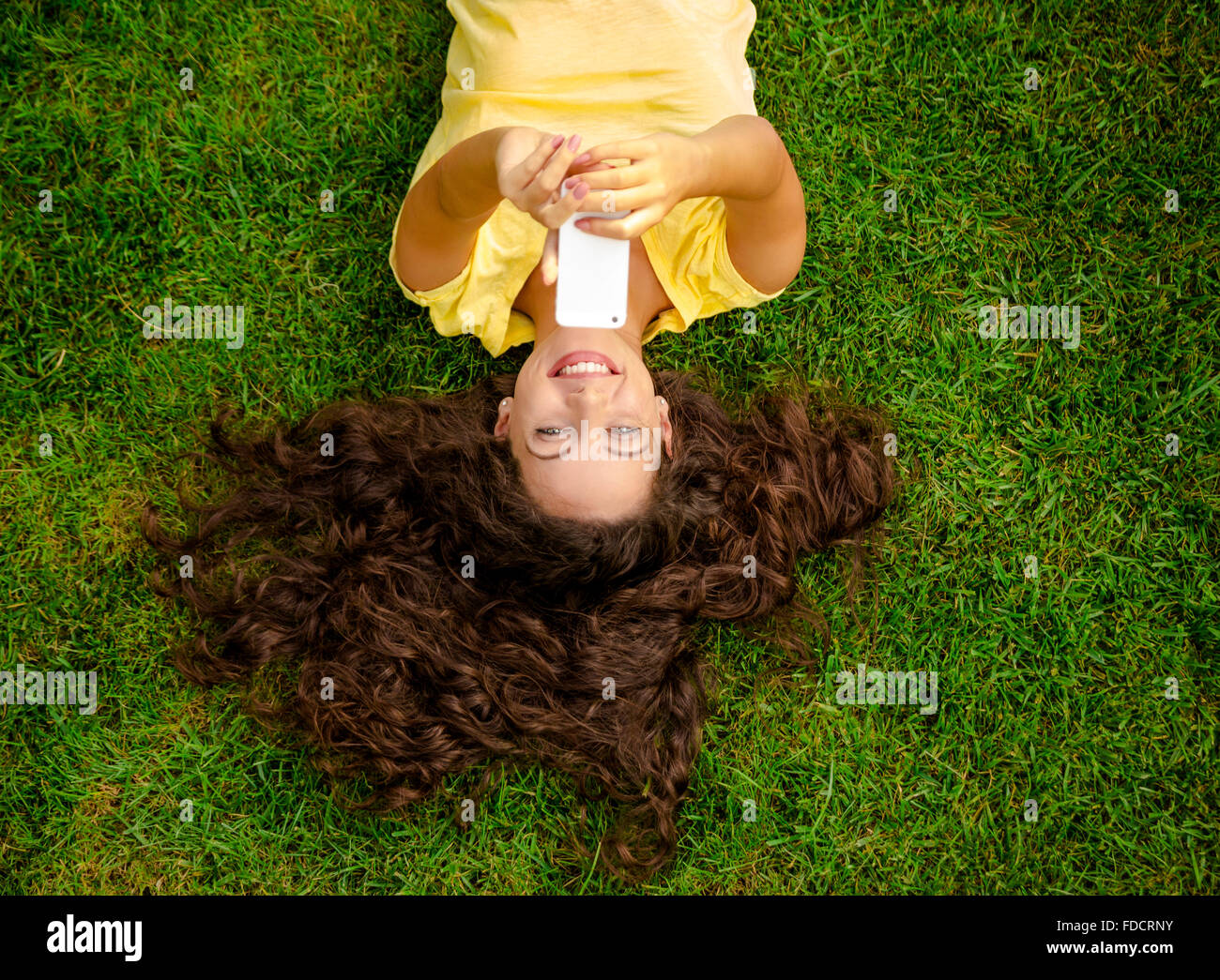 Lächelnde junge Frau auf dem Rasen liegen und ein Selbstporträt zu machen Stockfoto