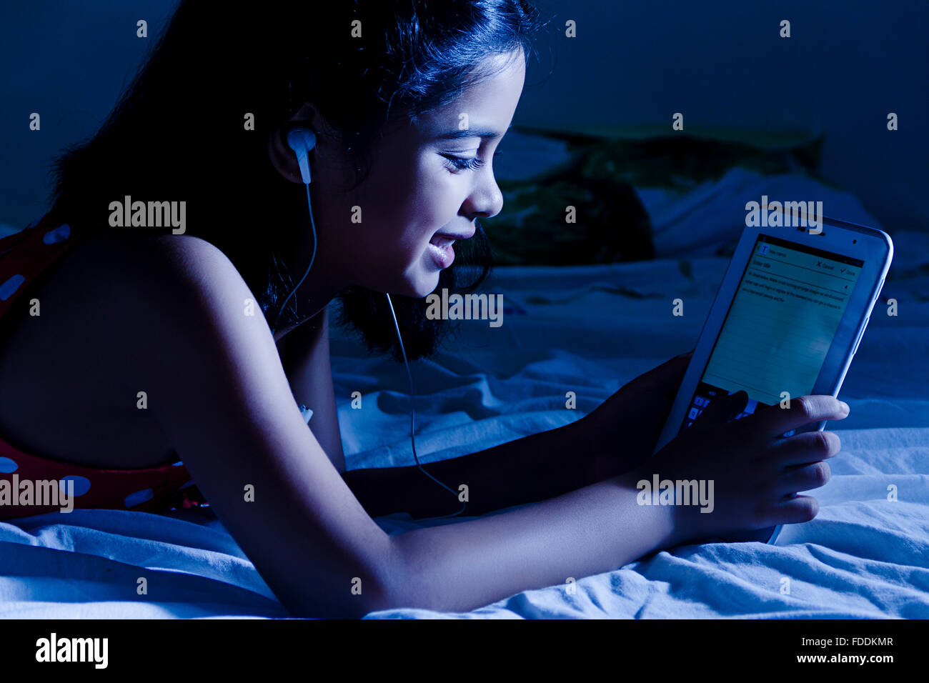 Ein Kind Mädchen Schlafzimmer Liegend Digital Tablet Messaging beobachten Stockfoto