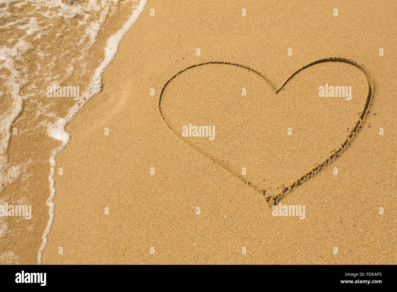 Herz am Strand Sand mit einer sanften Welle gezogen. Stockfoto