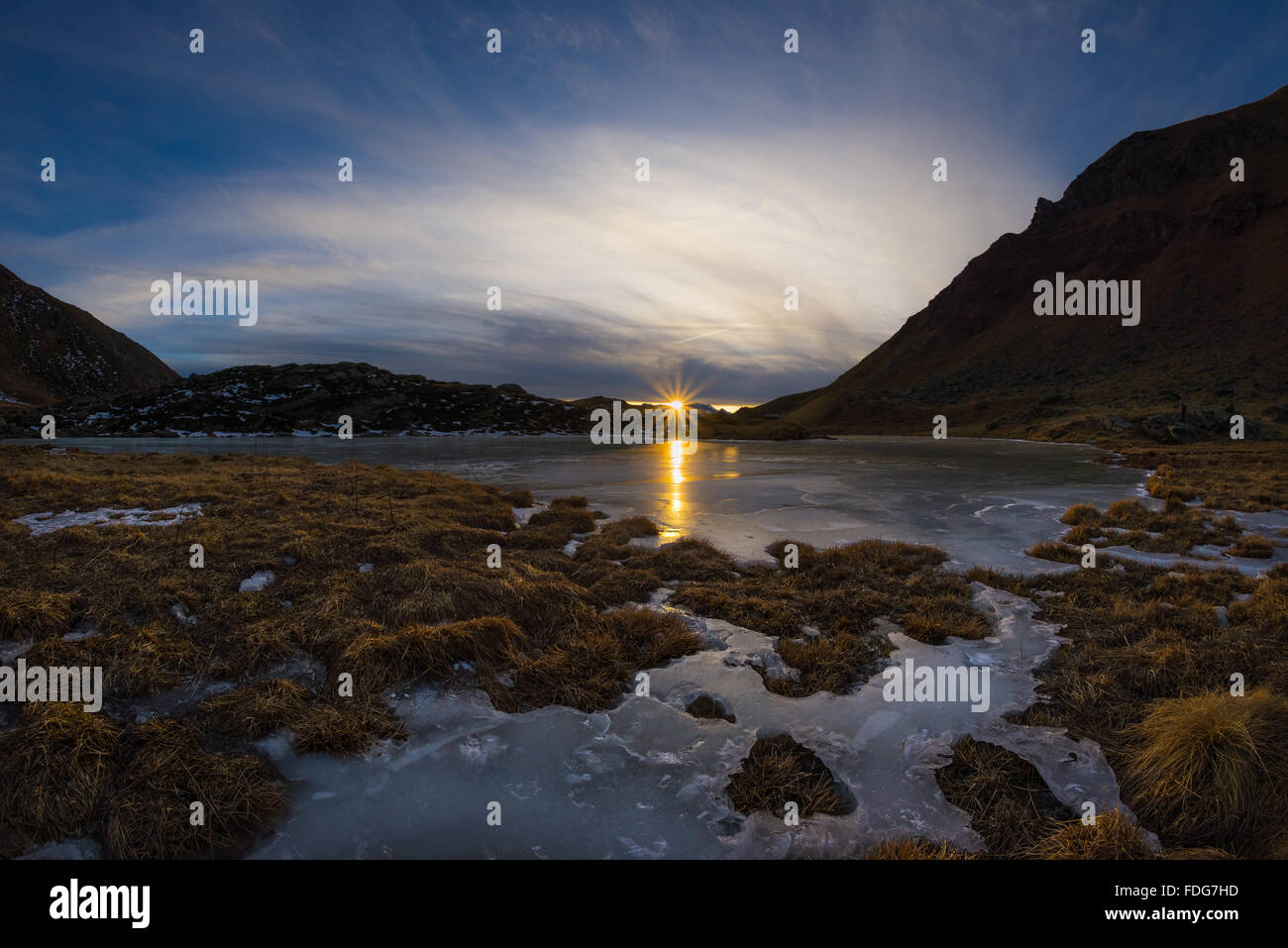 Hoch gelegenen Bergsee im idyllischen Land. Reflexion des Sonnenlichts auf die Eisfläche. Glühende Sunstar am Horizont bei s Stockfoto