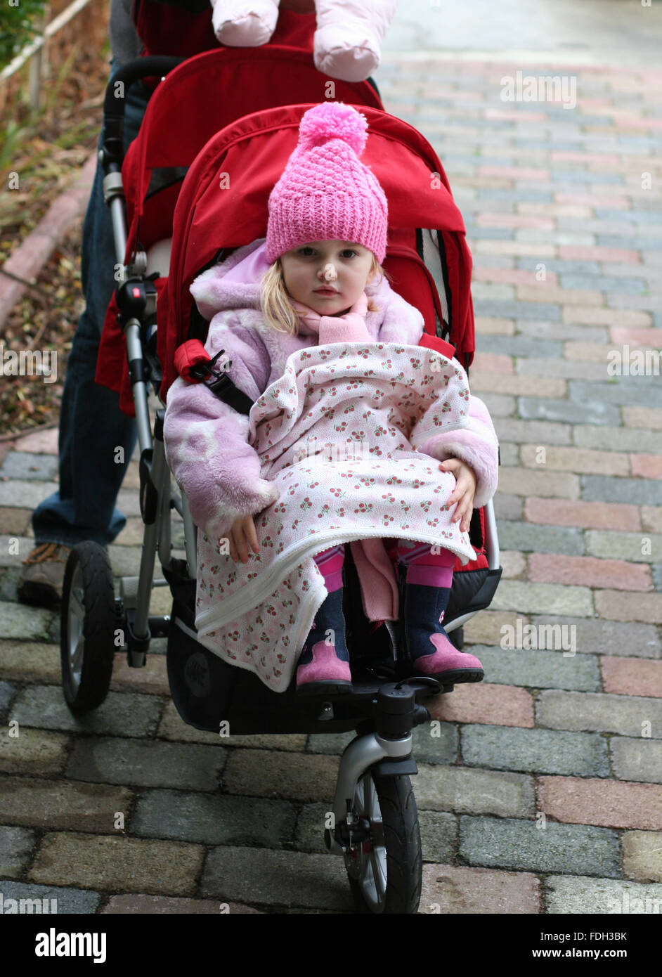 Kleines Mädchen, Kid, Kind trägt einen Winter bobble Hut in der Buggy mit  ihrer Decke gehen für einen Spaziergang an einem kalten Wintertag sitzt  Stockfotografie - Alamy