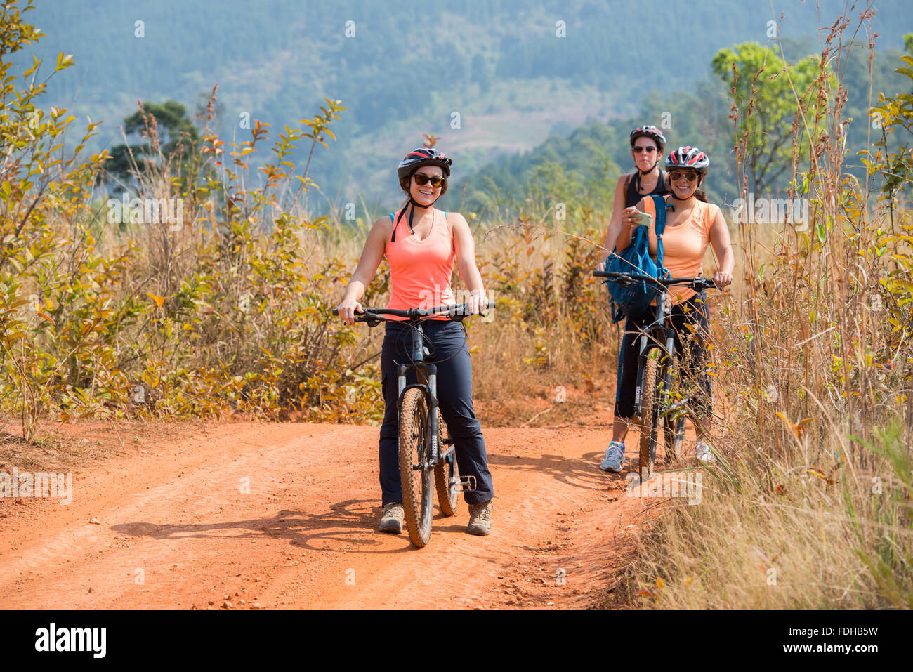 Drei Frauen Reiten Fahrräder auf einem Feldweg im Mlilwane Wildlife Sanctuary in Swasiland, Afrika. Stockfoto