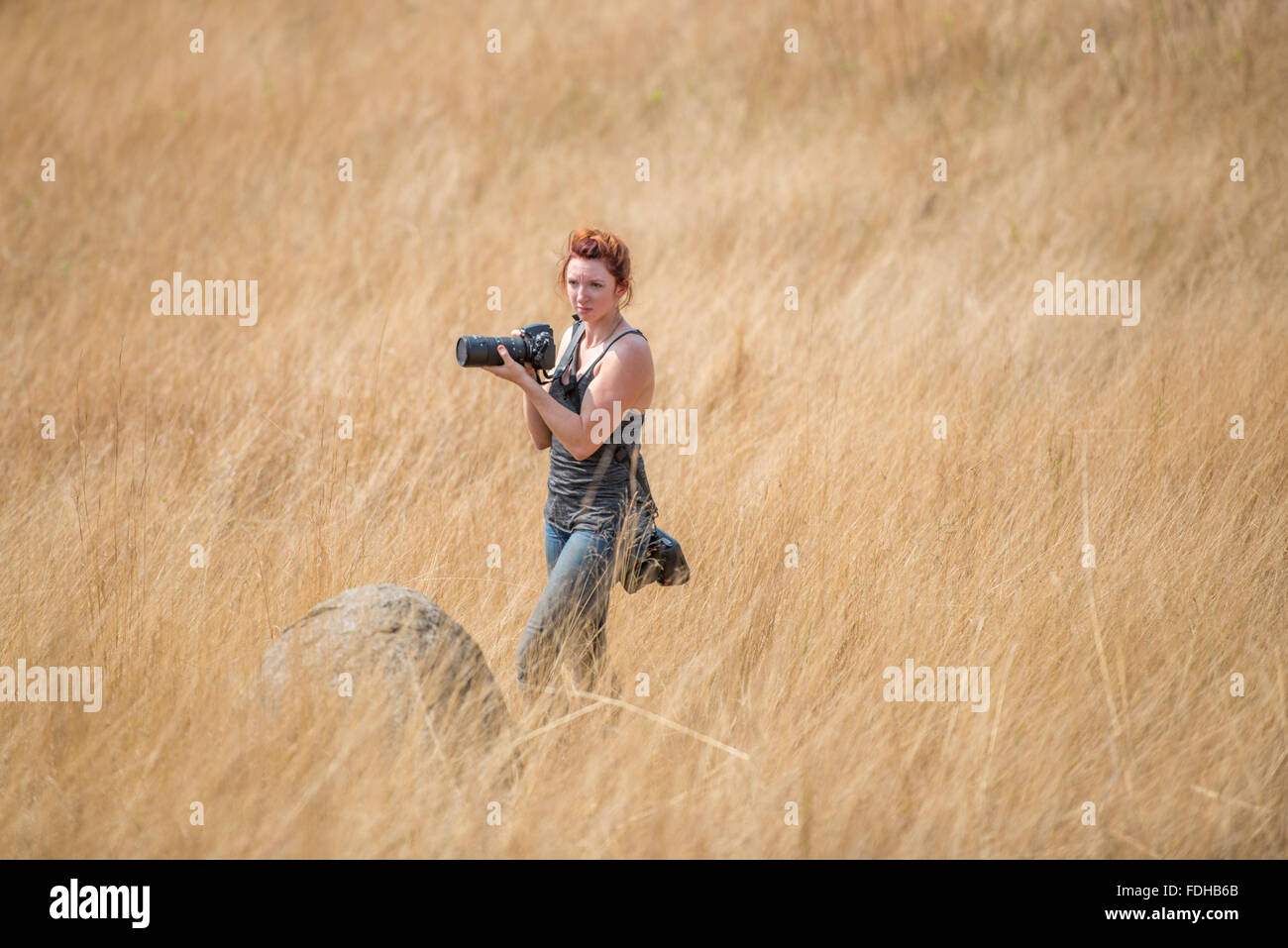 Rote Kopf Mädchen stehend mit Kameras mitten auf einem Feld im Mlilwane Wildlife Sanctuary in Swasiland, Afrika. Stockfoto