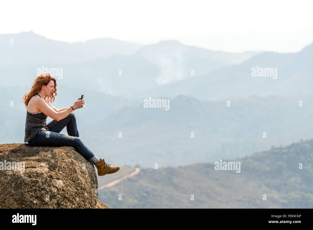 Rothaarige Mädchen sitzt auf dem Rand von einem Felsblock, der Aufnahme eines Fotos der Landschaft im Mlilwane Wildlife Sanctuary in Swasiland Stockfoto