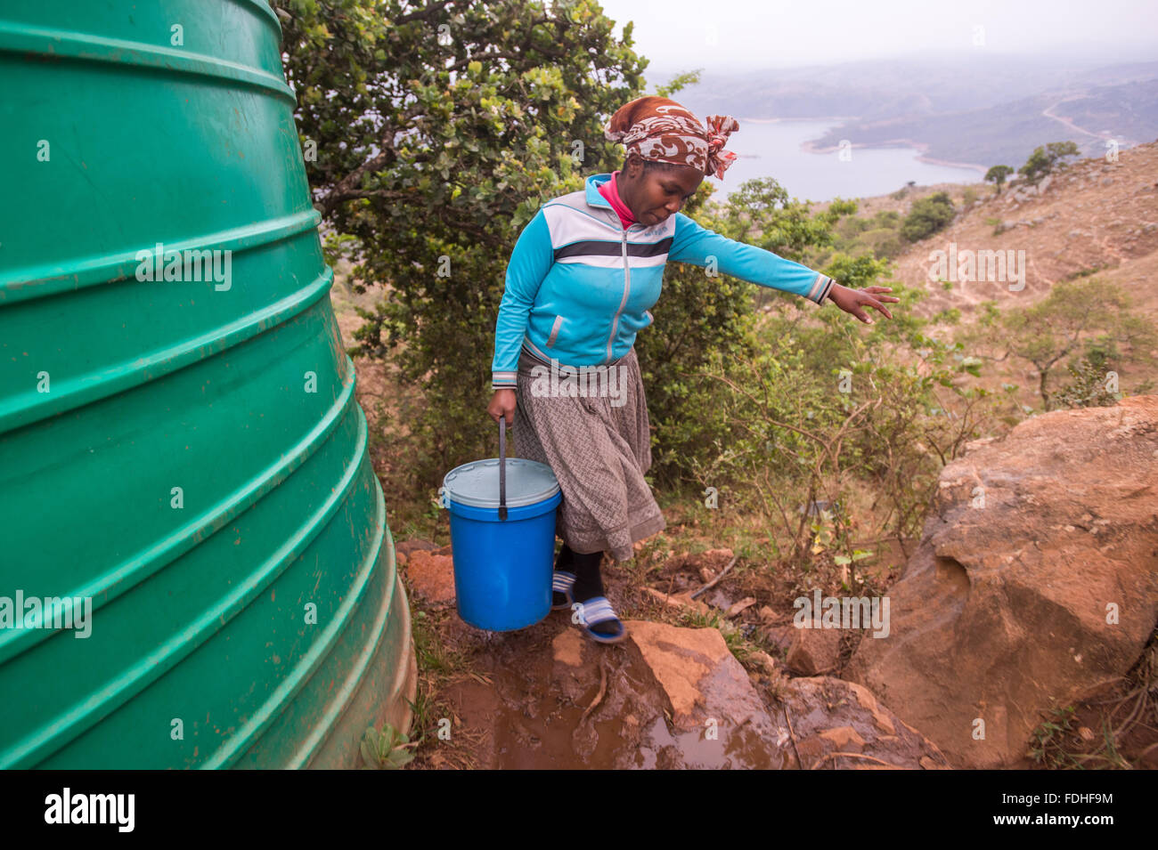 Frau, die trägt eines Eimers über felsiges Terrain in der Hhohho Region von Swasiland, Afrika. Stockfoto