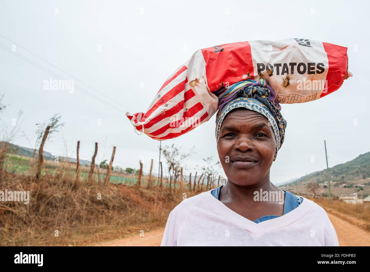 Frau ein Sack Kartoffeln auf dem Kopf auf einem Feldweg in der Hhohho Region von Swasiland, Afrika. Stockfoto