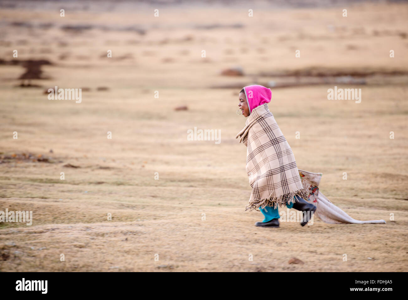 Junges Mädchen eingewickelt in eine Decke laufen durch eine weite Ebene in Sani Pass, Lesotho, Afrika. Stockfoto