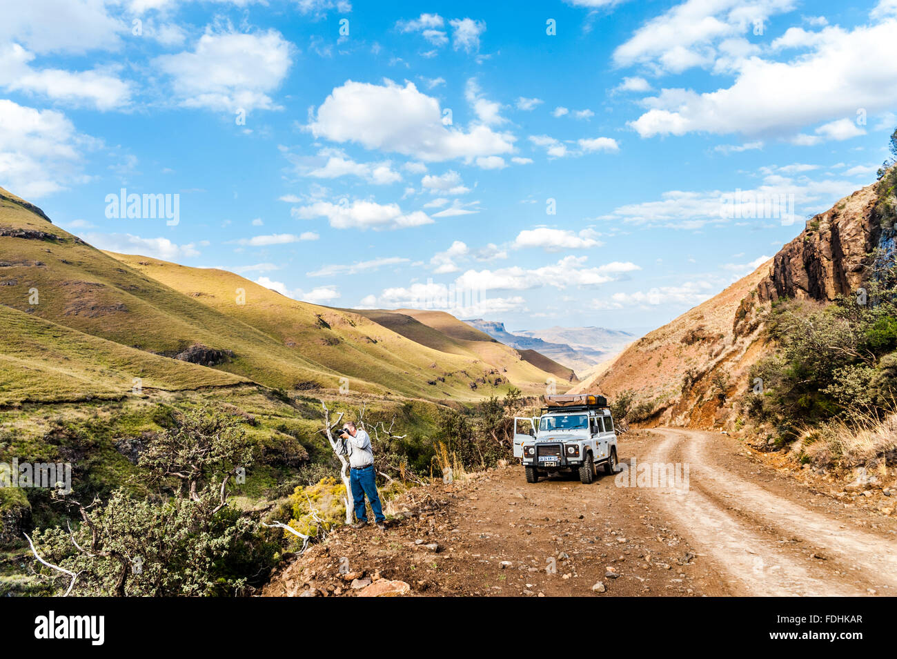 Land Rover Defender auf einer unbefestigten Straße geparkt und ein Mann fotografiert die Landschaft in Sani pass zwischen Südafrika und Lesotho Stockfoto