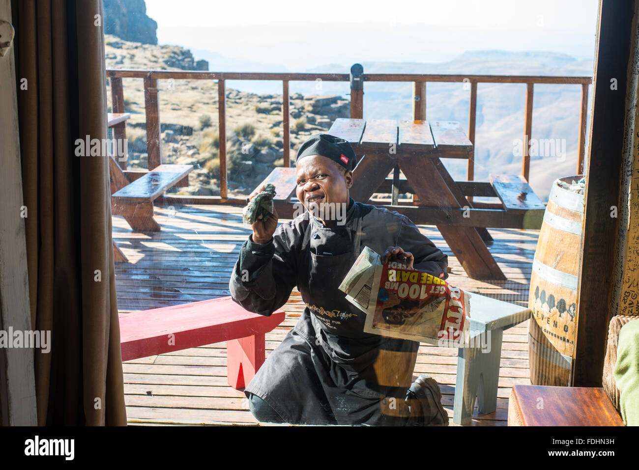 Einheimische Frau, die Reinigung der Fenster von Sani Top Lodge mit Zeitung in Lesotho, Afrika Stockfoto
