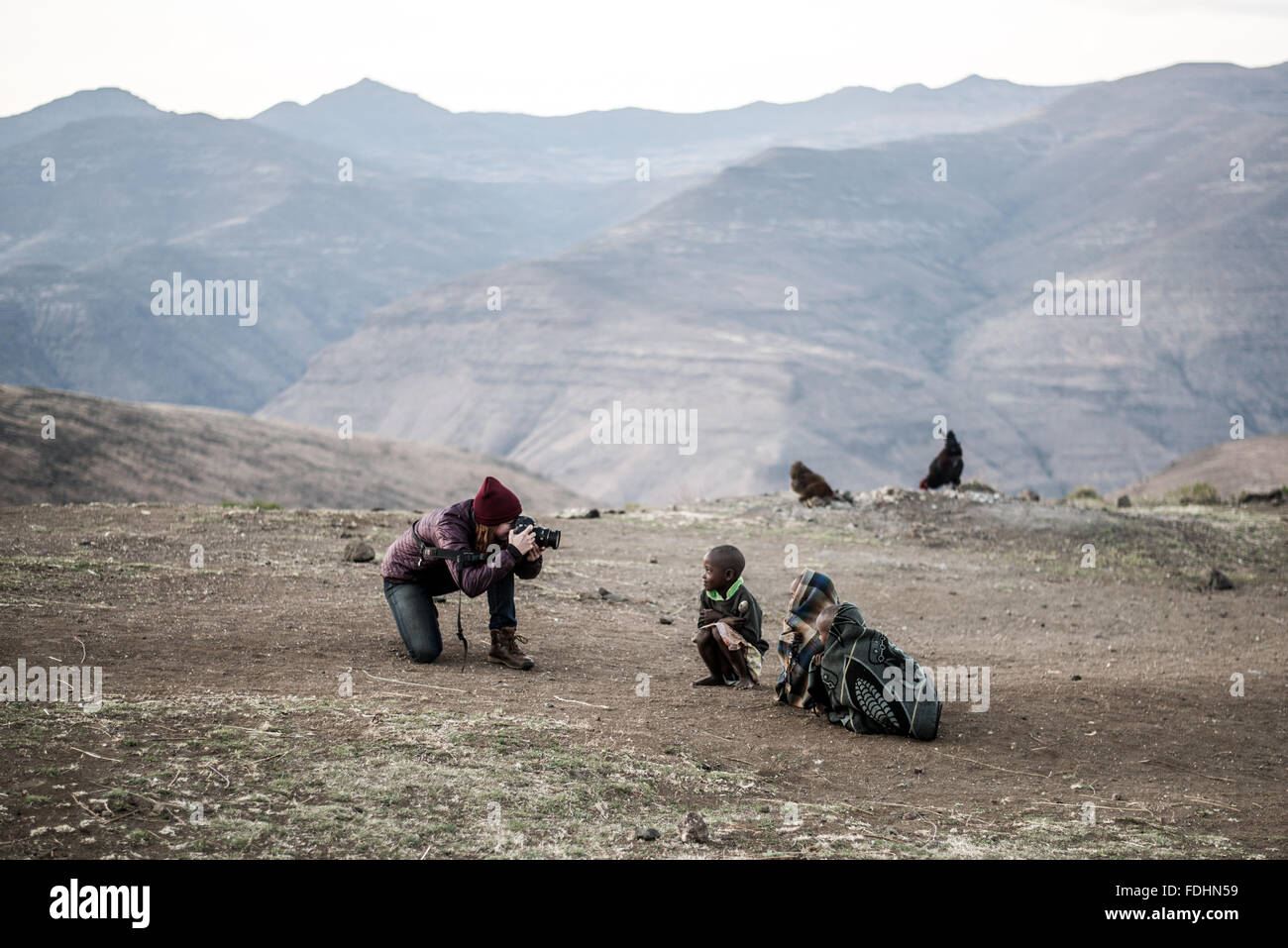 Junge Frau Touristen fotografieren von einheimischen Kindern eingewickelt in Decken in den Bergen von Lesotho, Afrika Stockfoto