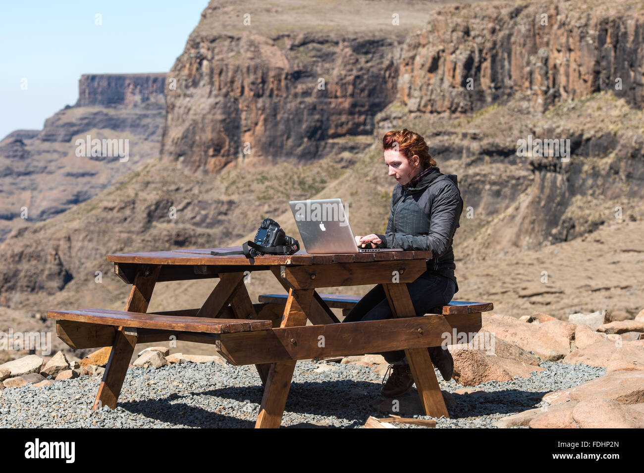 Junge Frau, die arbeitet auf ihrem Laptop an einem Picknicktisch in den Bergen von Lesotho, Afrika Stockfoto