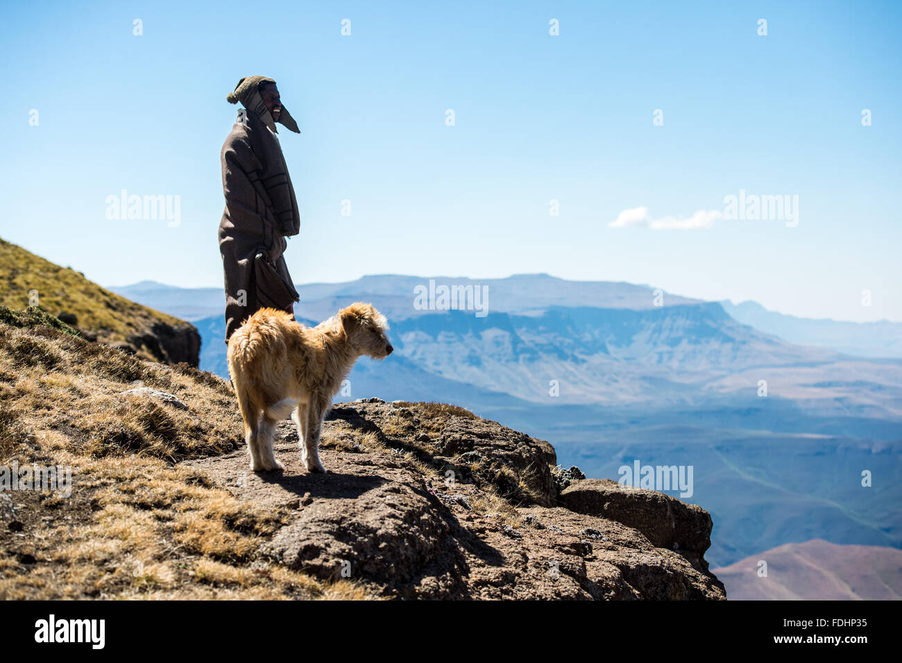 Hirte und sein Hund stand vor einer Bergkette eingewickelt in Decken in Lesotho, Afrika Stockfoto