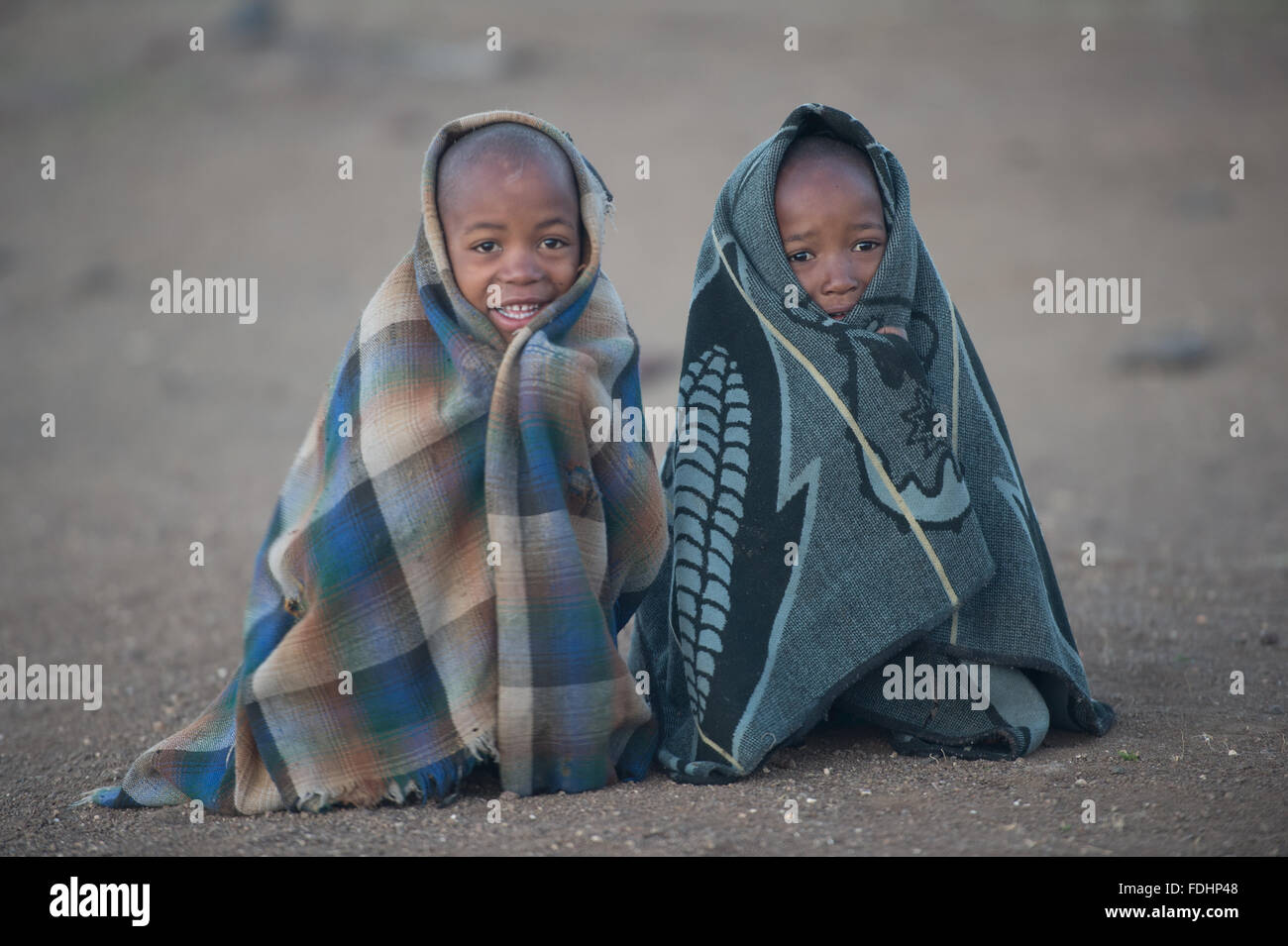 Zwei jungen in Decken gehüllt und sitzt auf den Schmutz Boden in Lesotho, Afrika Stockfoto