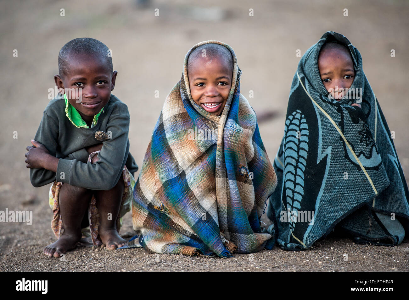 Drei junge Burschen in Decken gehüllt und sitzt auf den Schmutz Boden in Lesotho, Afrika Stockfoto