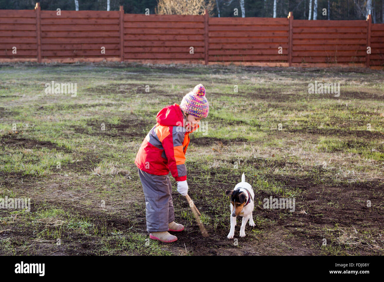 kleines Mädchen mit einem Hund spielen mit Holzstöcken Stockfoto