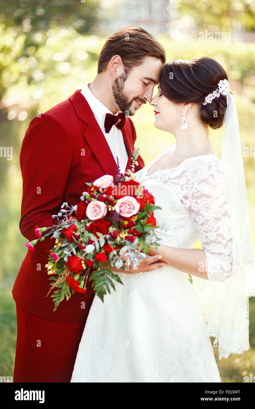 Marsala Brautpaar, Braut und Bräutigam umarmen, dunkelrote Farbe Stildesign. Anzug mit kastanienbraunen Fliege, weißes Kleid, Braut bo Stockfoto