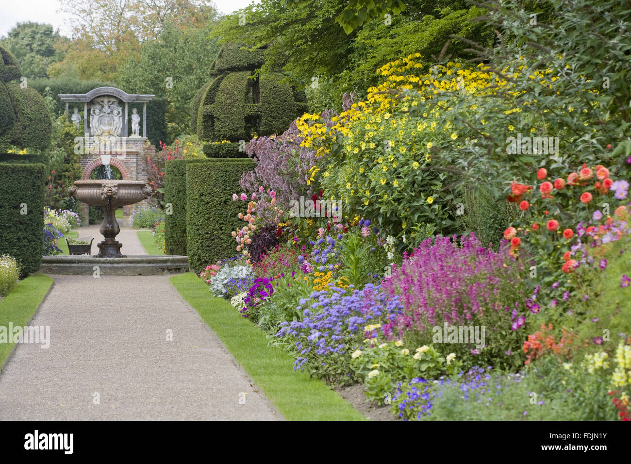 Blick in Richtung der roten italienischen Verona Marmor-Brunnen zwischen den doppelten Rahmen in der Wand-Garten im August bei Nymans, West Sussex. Der Brunnen wird durch Paare von Formschnitt Globen flankiert. Stockfoto