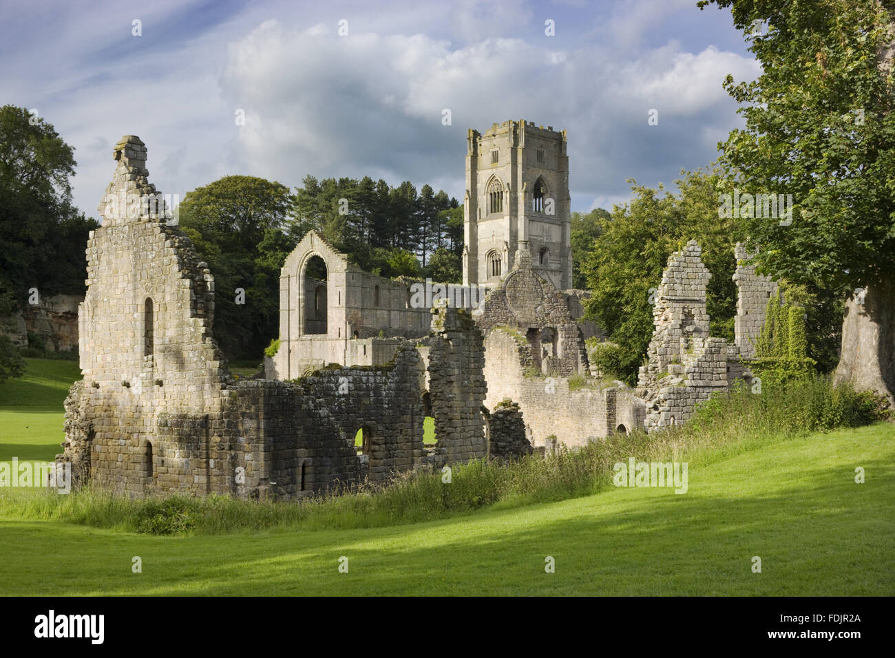 Die Ruinen der im Osten Guest House mit Turm von Fountains Abbey dahinter. Eine Zisterzienser-Gemeinschaft von Mönchen wurde hier in North Yorkshire im zwölften Jahrhundert bis zu seiner Auflösung im sechzehnten Jahrhundert gegründet. Stockfoto