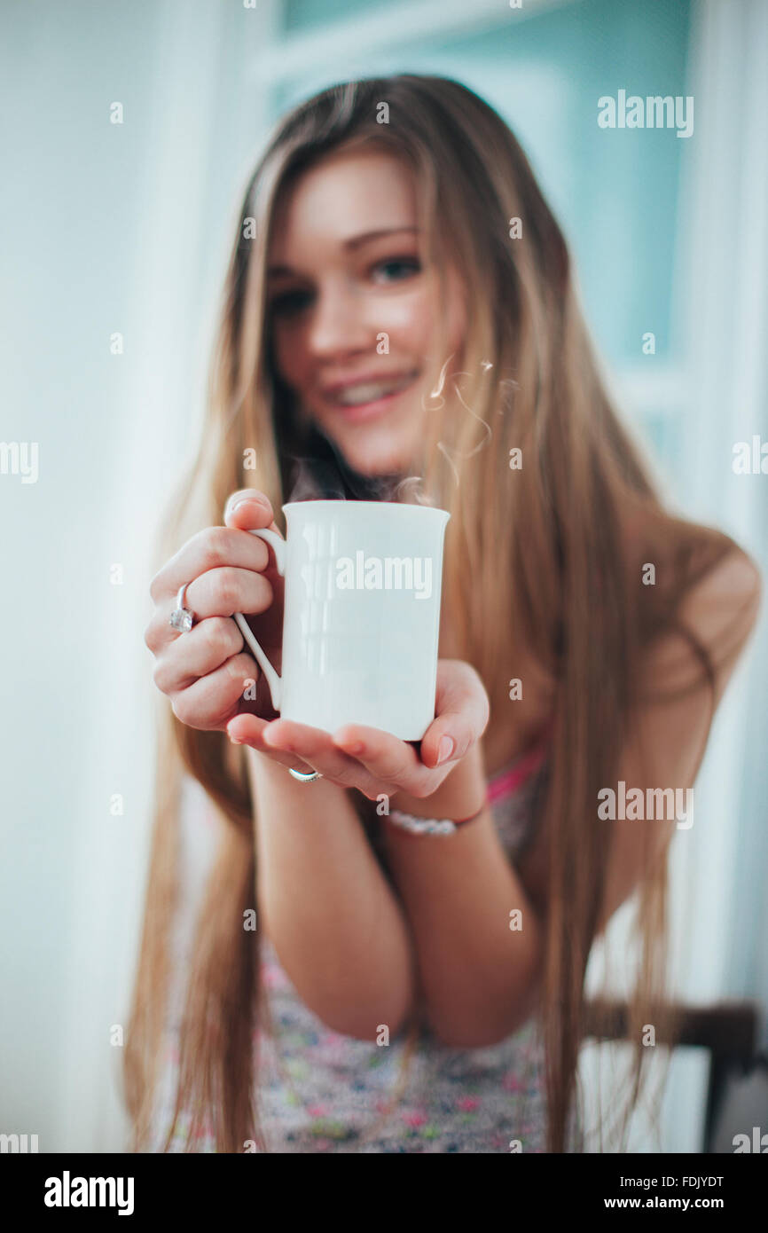 Lächelnde junge Frau hält einen Becher Kaffee Stockfoto