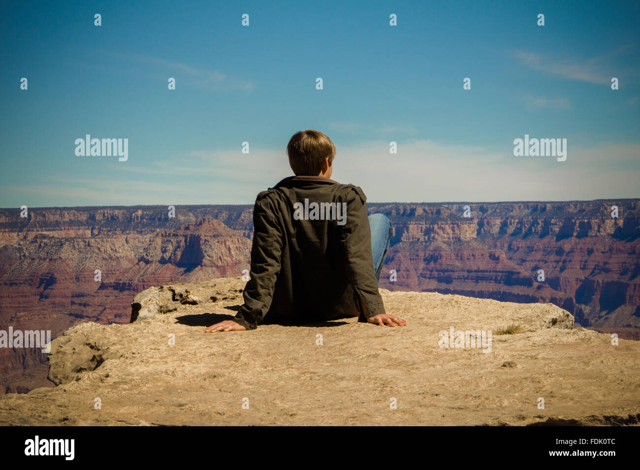 Rückansicht der ein junger Mann sitzt auf der Kante, Grand Canyon, Arizona, Amerika, USA Stockfoto