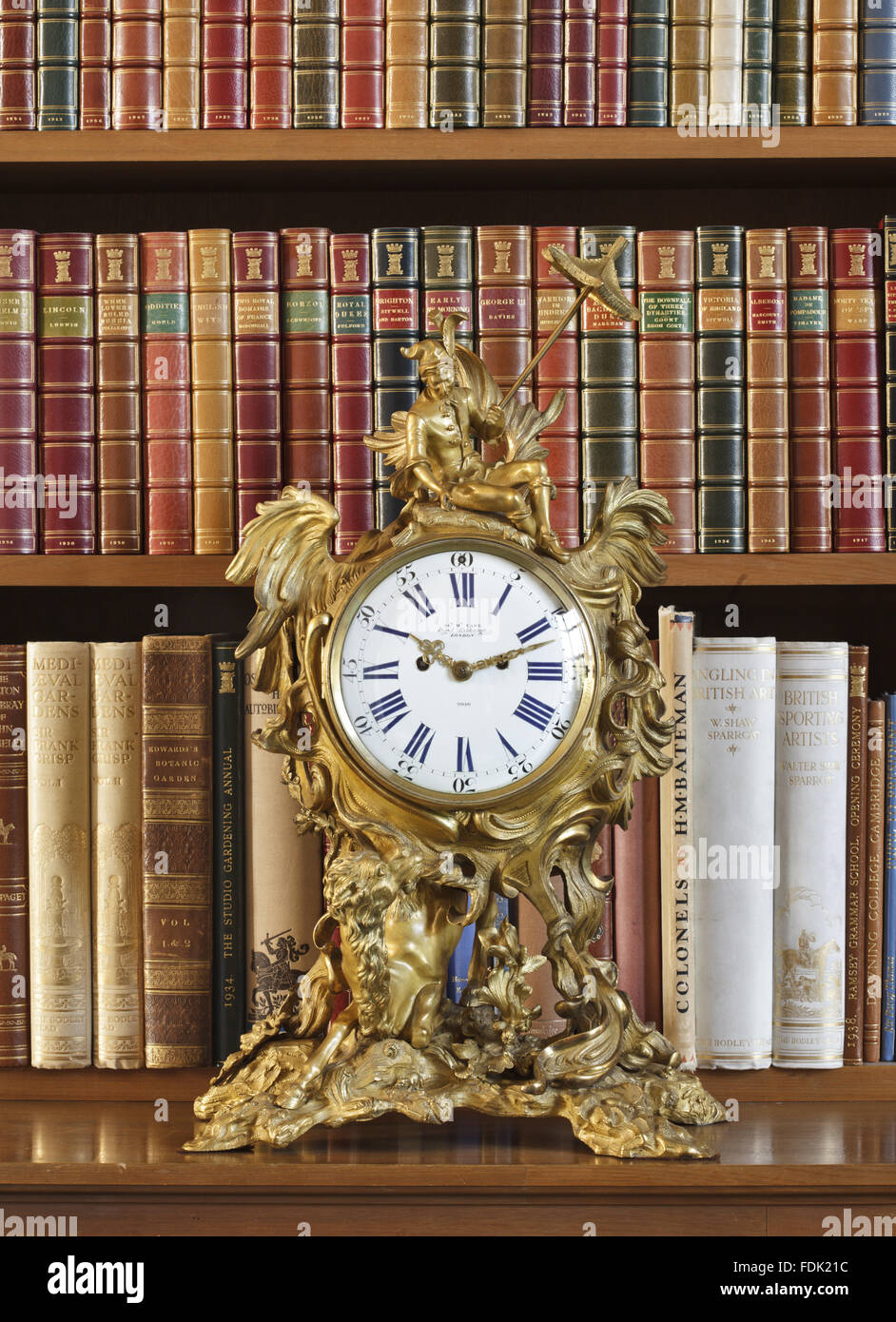 Messingbeschläge Uhr mit Leder gebundene Bücher in den Regalen in der Bibliothek in Anglesey Abbey, Cambridgeshire. Stockfoto