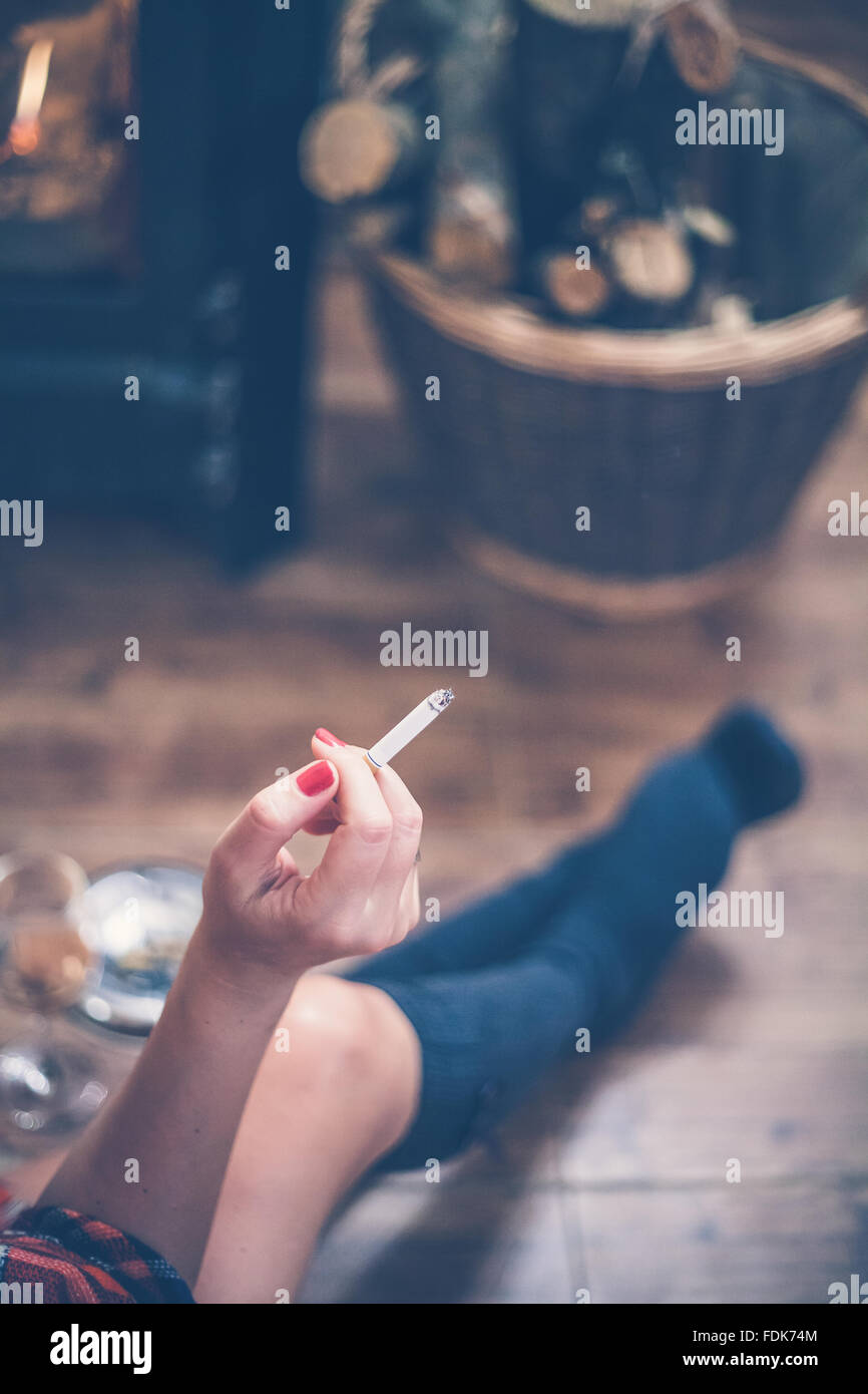 Frau sitzt vor Holzofen, eine Zigarette rauchend Stockfoto