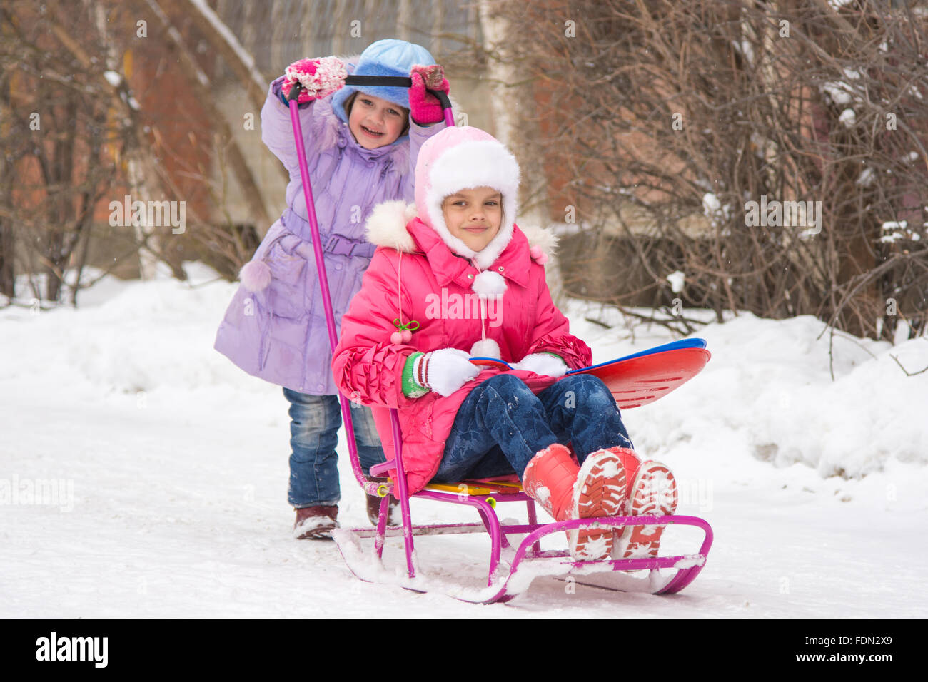 Zwei Mädchen Freundinnen fahren einander auf einem Schlitten in den schneereichen Winterwetter Stockfoto