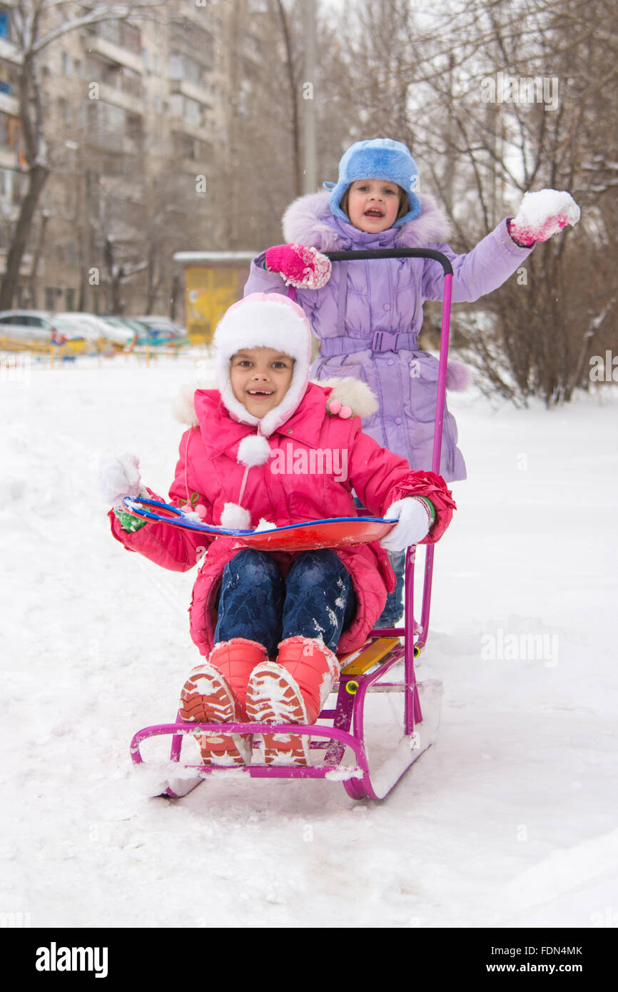 Zwei Mädchen Freundinnen fahren einander auf einem Schlitten in den schneereichen Winterwetter Stockfoto