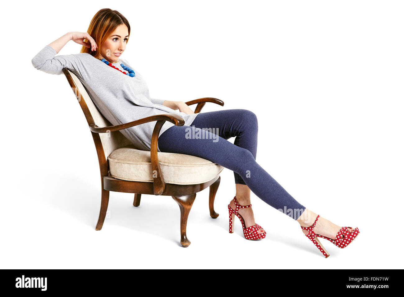 Junge Frau sitzt auf einem Stuhl Oldschool mit gezogenen Bein entspannt und fröhlich lächelnd. Stockfoto