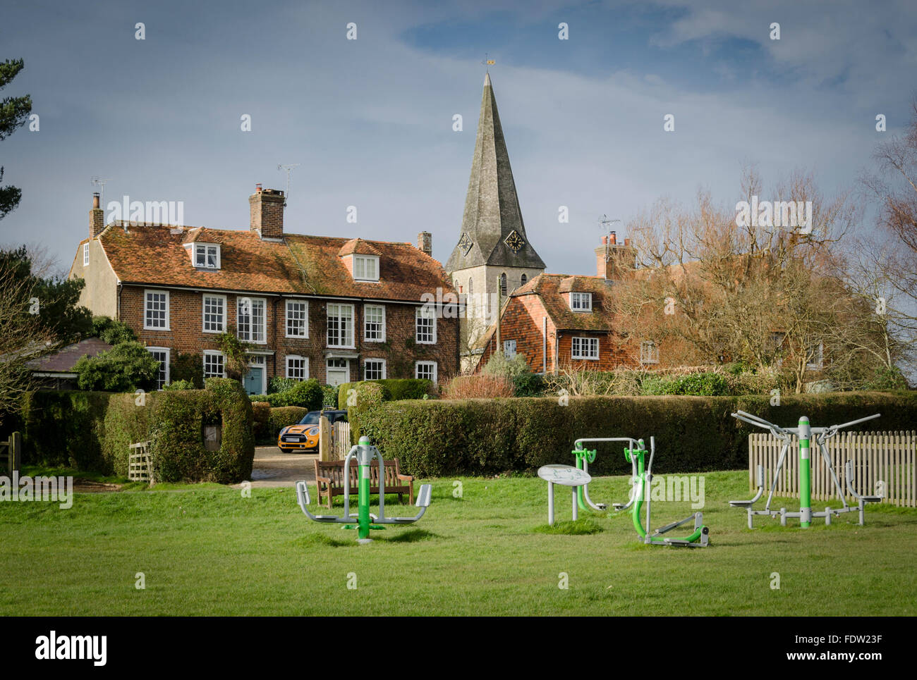 Sportgeräte auf Woodchurch Dorfplatz, Kent, UK, mit All Saints Church und Backstein und gekachelte Häuschen im Hintergrund Stockfoto
