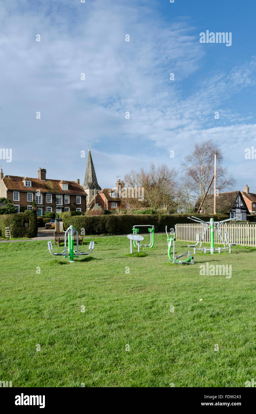 Sportgeräte auf Woodchurch Dorfplatz, Kent, UK, mit All Saints Church und Backstein und gekachelte Häuschen im Hintergrund Stockfoto