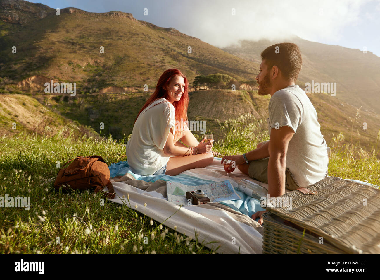 Junger Mann und Frau sitzen auf dem Rasen bei einem Picknick mit Glas Wein. Junges Liebespaar, ein Gespräch während auf Stockfoto