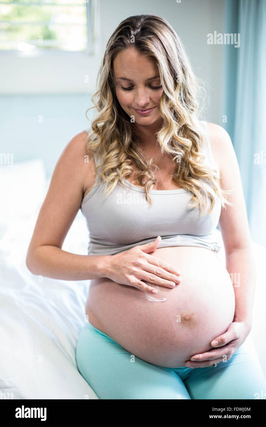 Schwangere Frau, die Sahne auf den Bauch Stockfoto