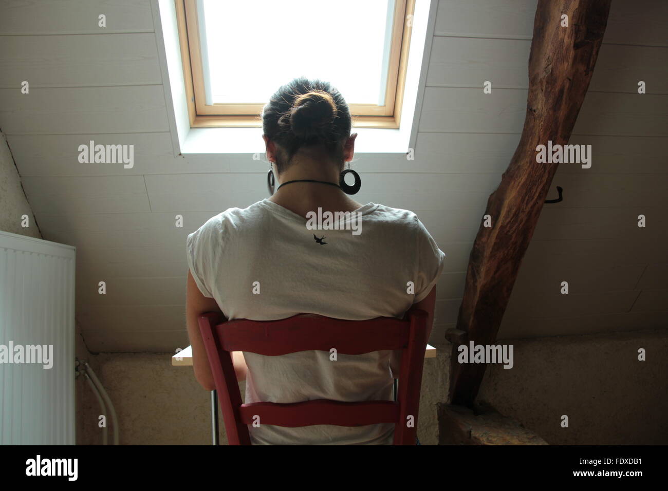 Frau unter dem Fenster auf einem Stuhl sitzend Stockfoto