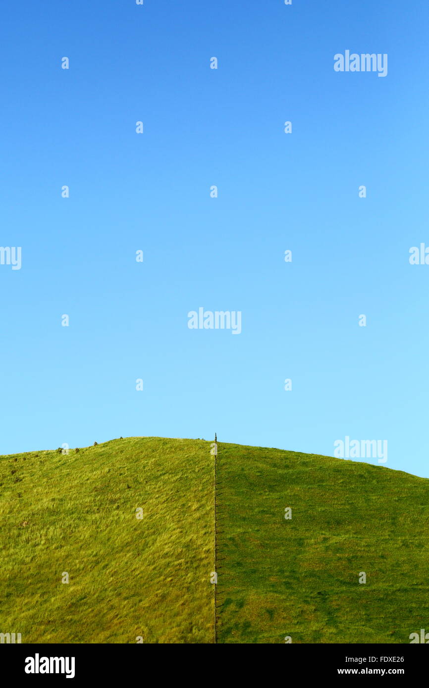 Ein Zaun halbiert einen grasbewachsenen Hügel unter einem strahlend blauen Himmel - es scheint, dass der Rasen in der Tat grüner auf der anderen Seite werden kann. Stockfoto