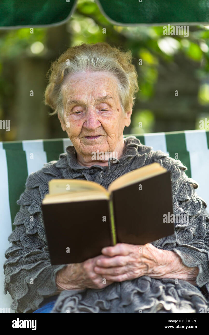 Eine ältere Frau liest das Buch in der Laube sitzen. Stockfoto