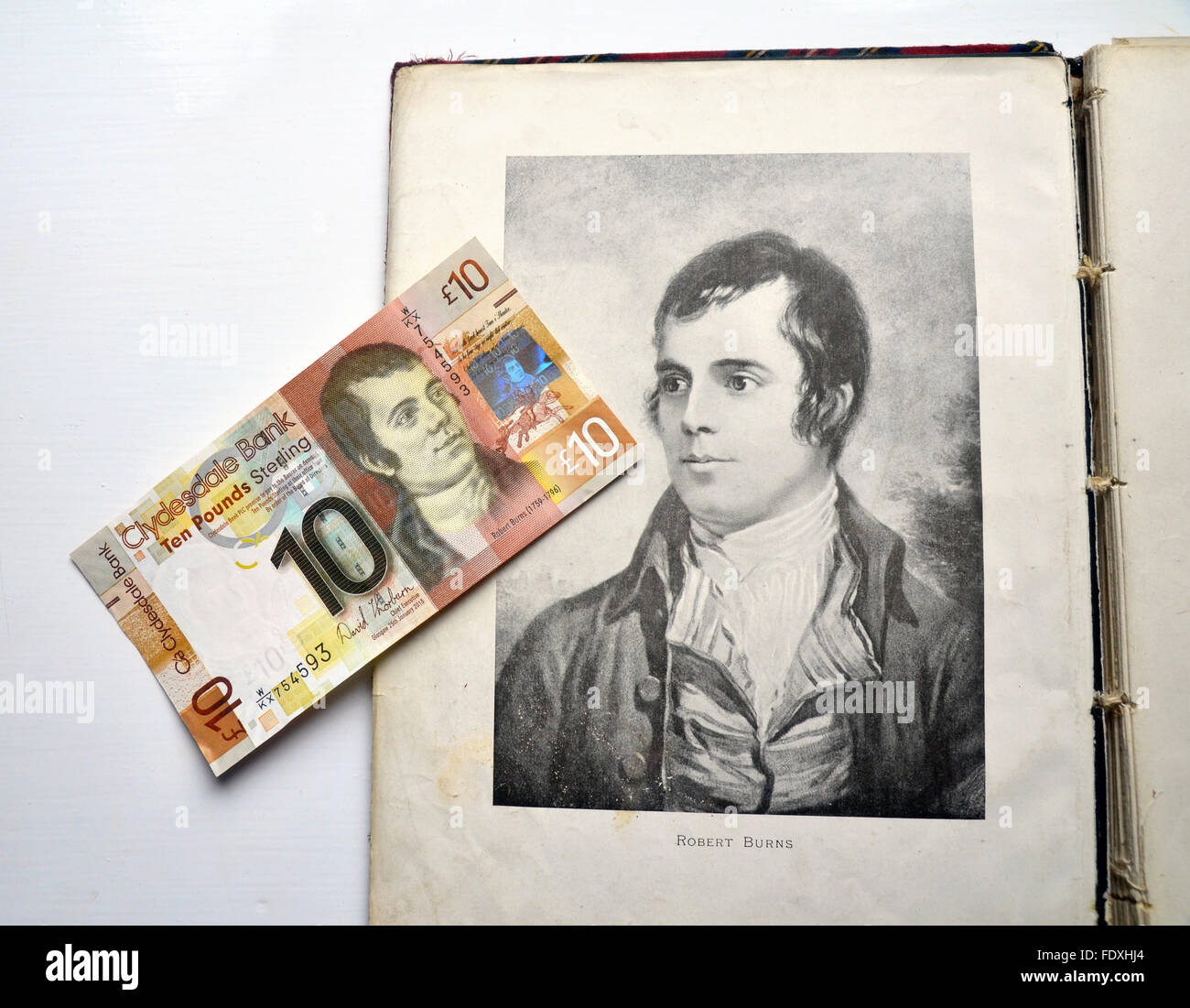 Zehn-Pfund-Note mit Portrait von Robert Burns liegen oben auf ein Portrait von ihm illustrierte in einem alten Buch. Stockfoto