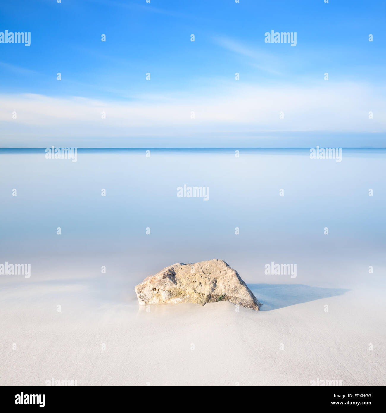 Ein Felsen auf einem weißen Sandstrand und blauen Meer am Horizont. Langzeitbelichtung Fotografie. Stockfoto