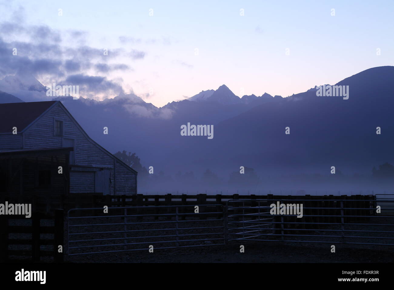 Bauernhof Schuppen im Nebel als Dämmerung steigt hinter der südlichen Alpen, einschließlich Aoraki / Mount Cook, an Fox Glacier, Neuseeland. Stockfoto